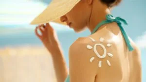 una donna in spiaggia con un cappello di paglia e la crema solare sulle spalle ad indicare l'importanza di una adeguata protezione